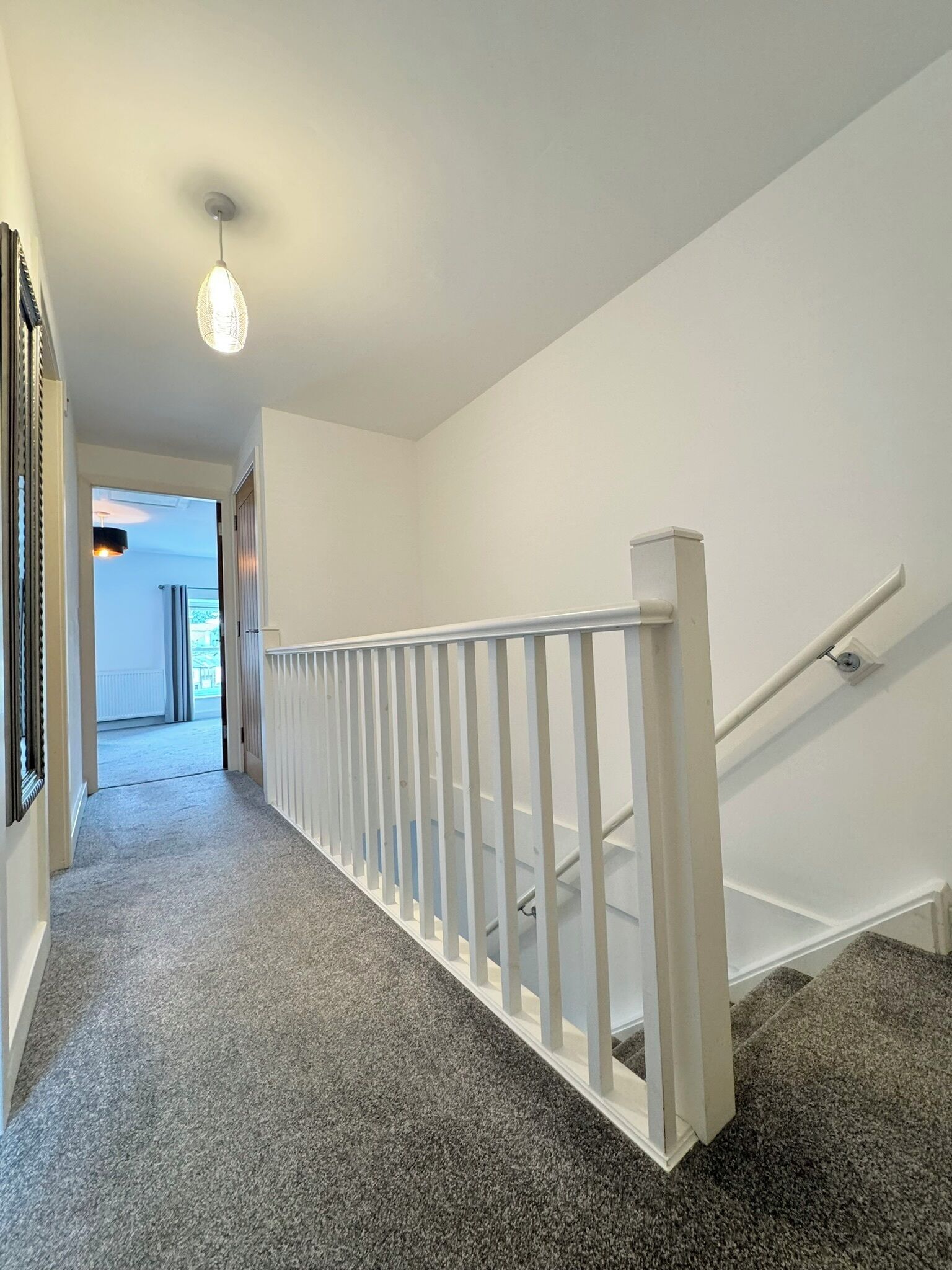 Un couloir avec une rambarde blanche, un sol recouvert de moquette et un luminaire au plafond.
