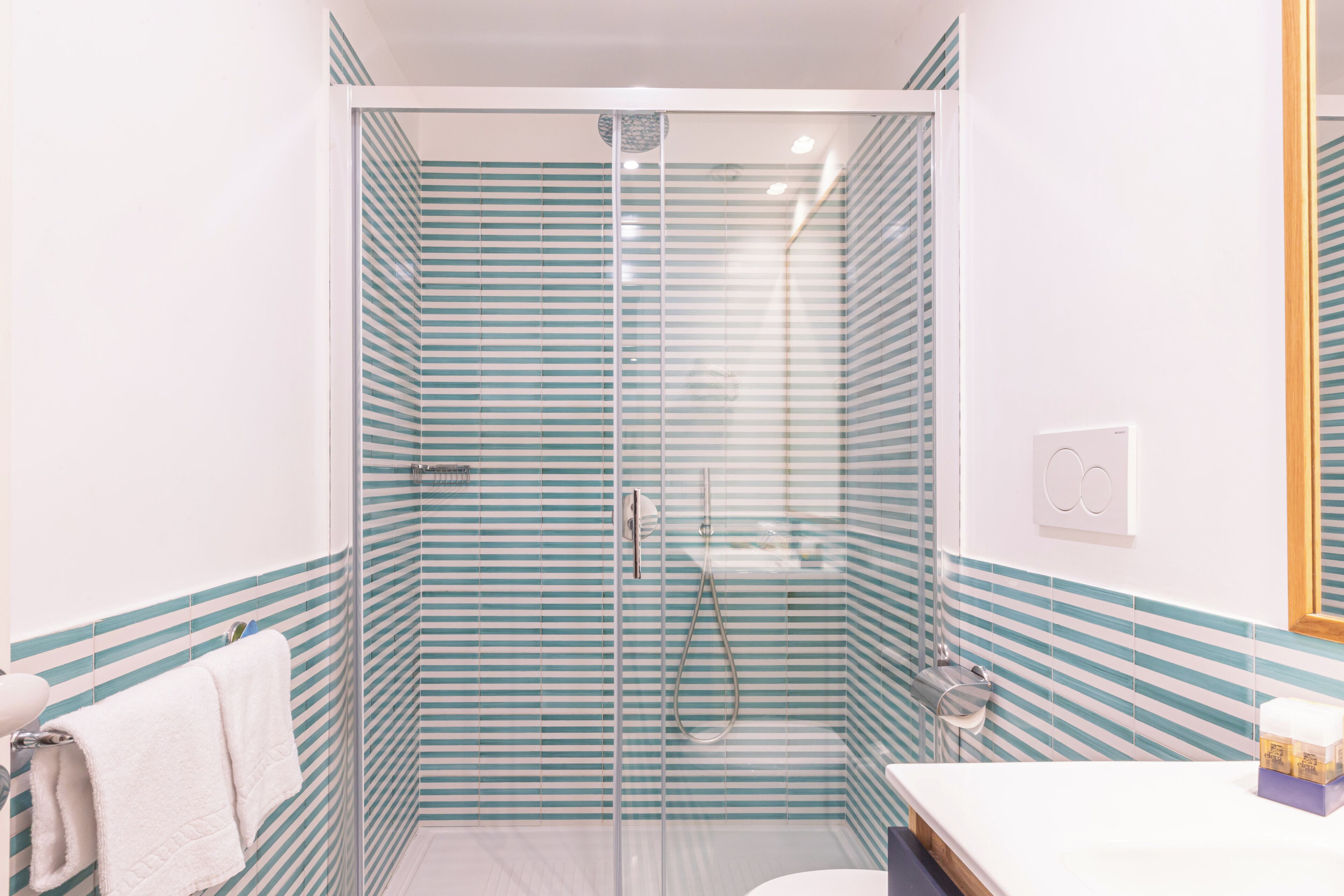 Un baño con ducha vidriada, azulejos verticales a rayas, un lavamanos blanco y un espejo.