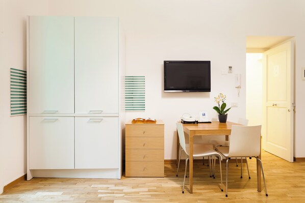 Une chambre comprenant une armoire, un bureau avec une chaise, une télévision et une plante en pot.