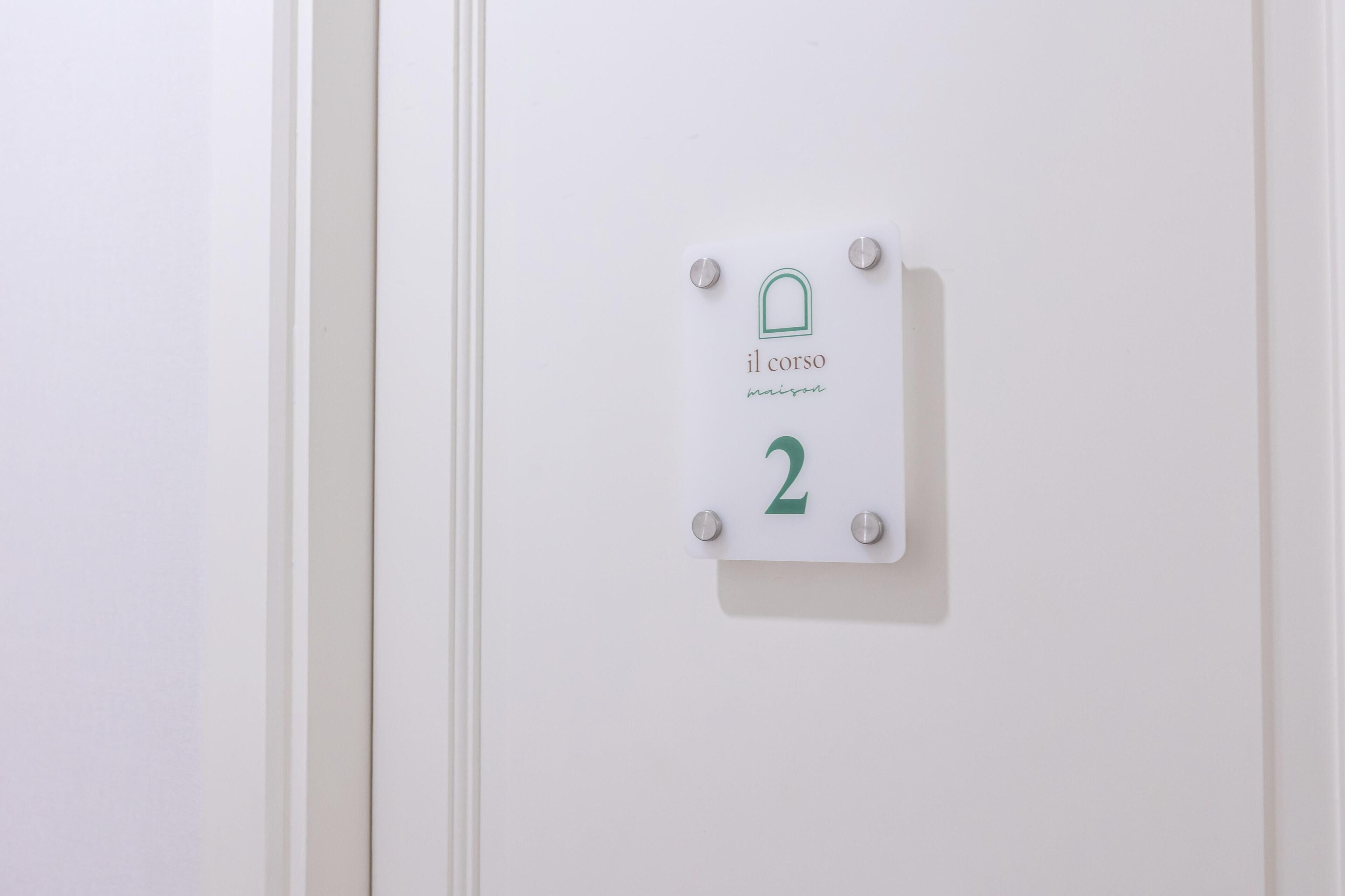 A white door with a sign indicating room number 2, labeled 'il corso' and 'maison.'