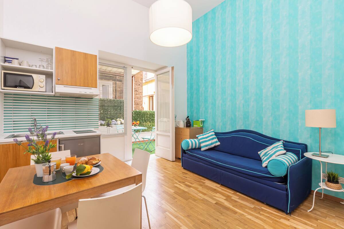 A compact living space with a kitchenette, a dining area, a sofa, and a small table with a lamp.