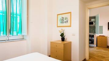 Un dormitorio con una cama, un aparador de madera, una planta en maceta y un cuadro en la pared.