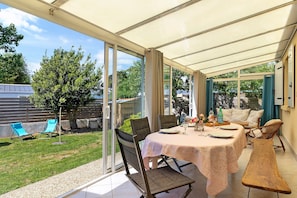 A covered patio with a table set for dining, chairs, and a bench.