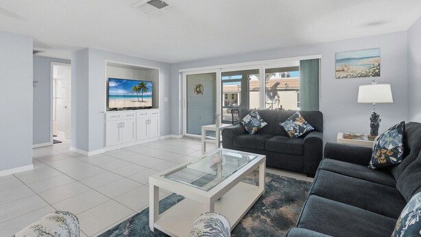 A modern living room with a flat-screen TV, a sofa, a coffee table, and a view of the outdoors through large windows. - Villa 13 Island House (Sarasota)