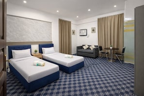 Une chambre d’hôtel avec deux lits, un canapé, une petite table avec des chaises et un téléviseur fixé au mur.