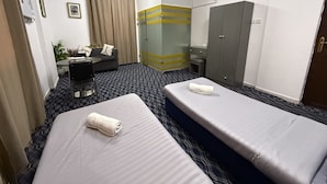 Habitación de hotel con dos camas, un escritorio, un armario y un baño con mampara de vidrio.