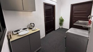 Una kitchenette compacta con microondas, hervidor y un lavamanos pequeño.