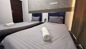 Habitación de hotel con dos camas individuales, cada una con una toalla enrollada, una mesita de noche pequeña y una planta en maceta.