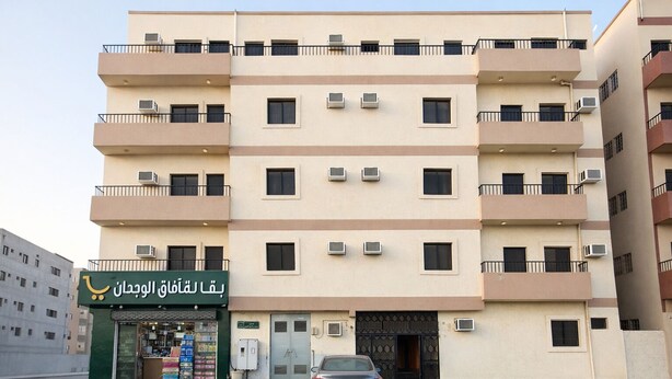 Un edificio residencial de varios pisos con balcones, unidades de aire acondicionado y una tienda con letreros en árabe.