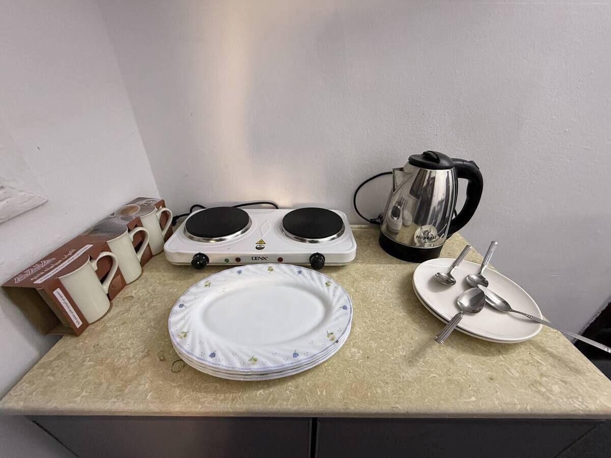 A kitchen counter with a stove, a kettle, a plate, and a mug set.