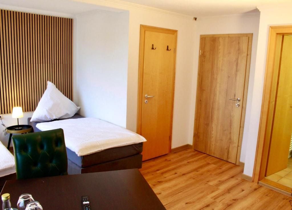 Quarto de hotel com cama, escrivaninha, cadeira e duas portas de madeira.