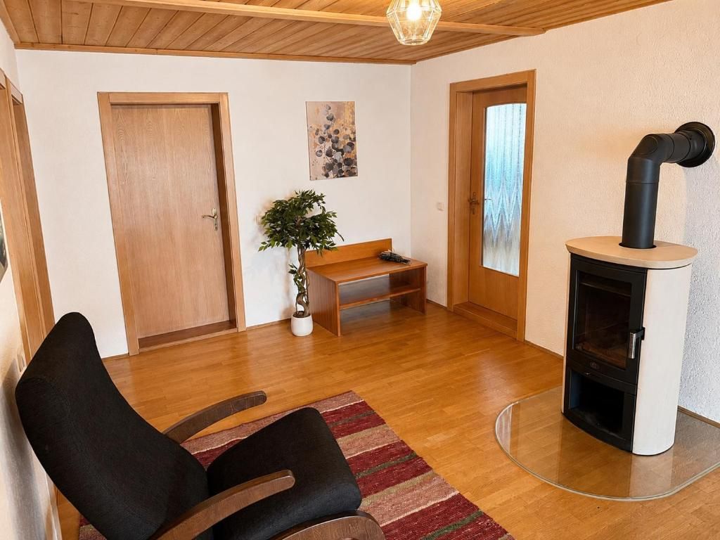 A room with a wooden floor, a black chair, a bench, a small table, a potted plant, a fireplace, and a door.