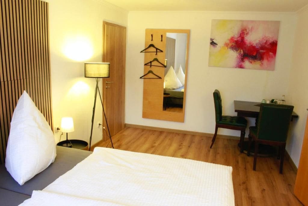Ein Hotelzimmer mit Bett, Schreibtisch, Stuhl, Lampe, Spiegel und einem Bild an der Wand.