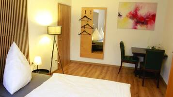Ein Hotelzimmer mit Bett, Schreibtisch, Stuhl, Lampe, Spiegel und einem Bild an der Wand.