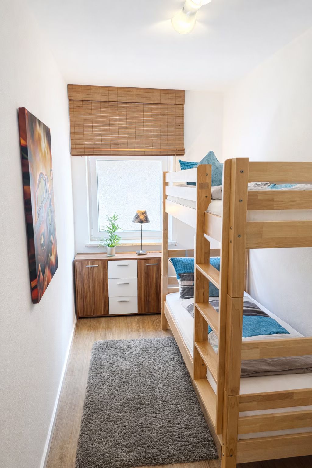 Habitación pequeña con una litera, un escritorio con una planta y una ventana con persianas.
