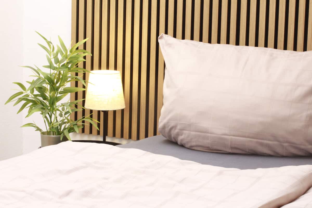 Ein ordentlich bezogenes Bett mit Kissen und einer Lampe daneben.