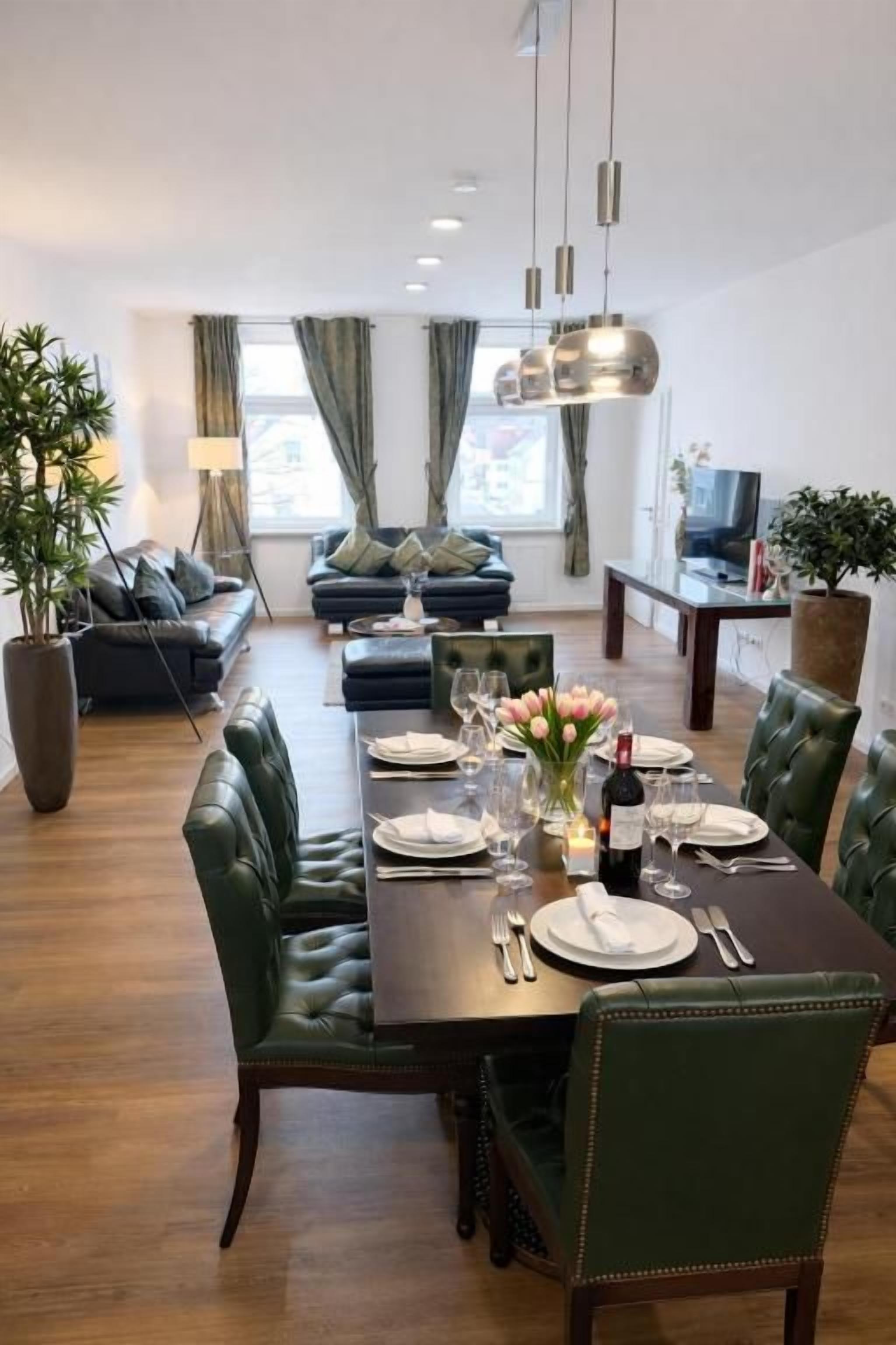 En matplats med ett bord dukat för fyra personer, omgiven av grönt klädda stolar.