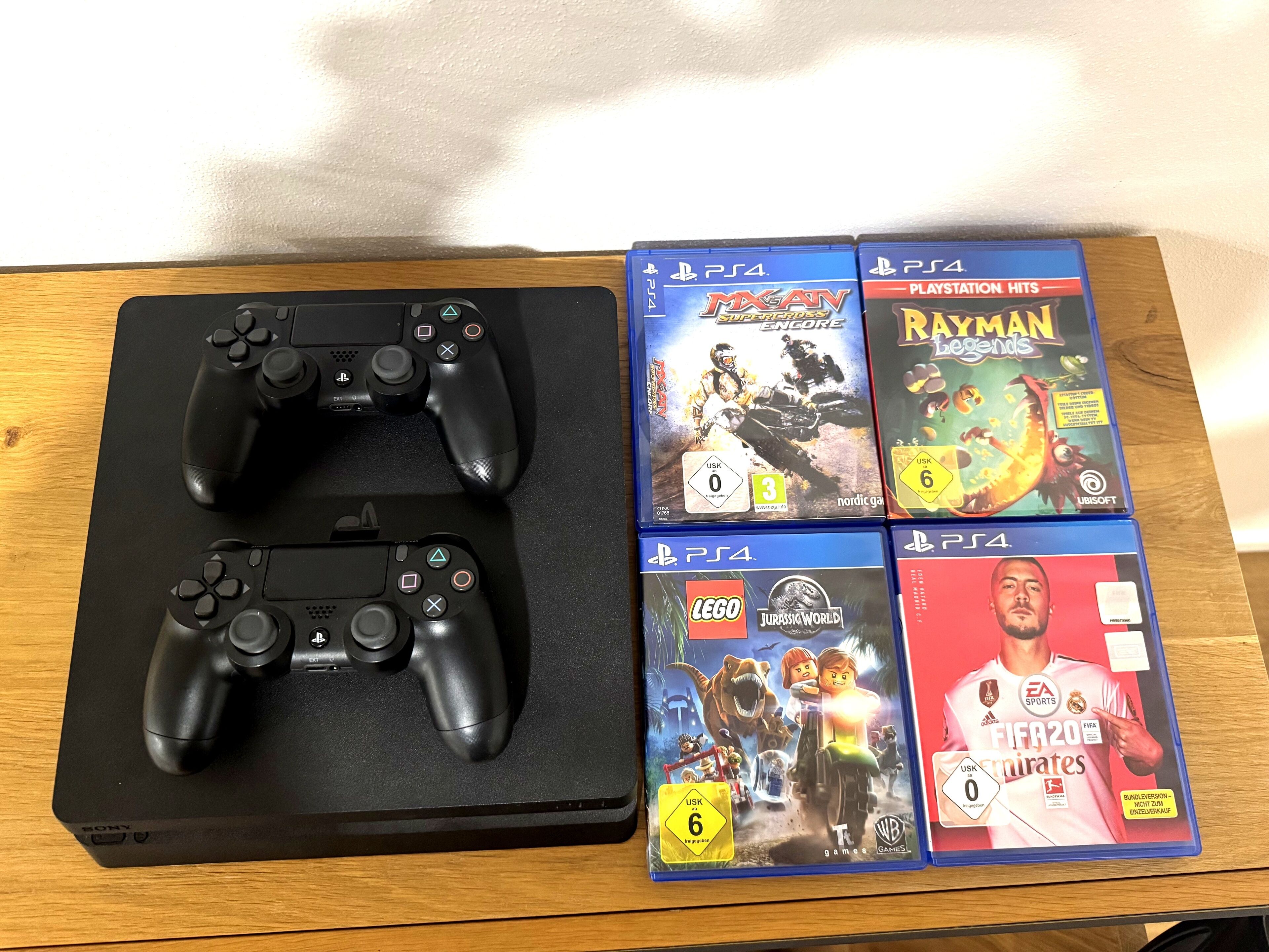 Una mesa de madera con dos controles negros de Sony PlayStation y cuatro cajas de videojuegos para PlayStation 4.