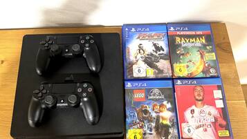 Una mesa de madera con dos controles negros de Sony PlayStation y cuatro cajas de videojuegos para PlayStation 4.