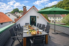A rooftop dining area with a table set for six, surrounded by chairs, and an umbrella providing shade. - Gästehaus Jekle – Zimmer & Ferienwohnungen (Neuburg an der Kammel)