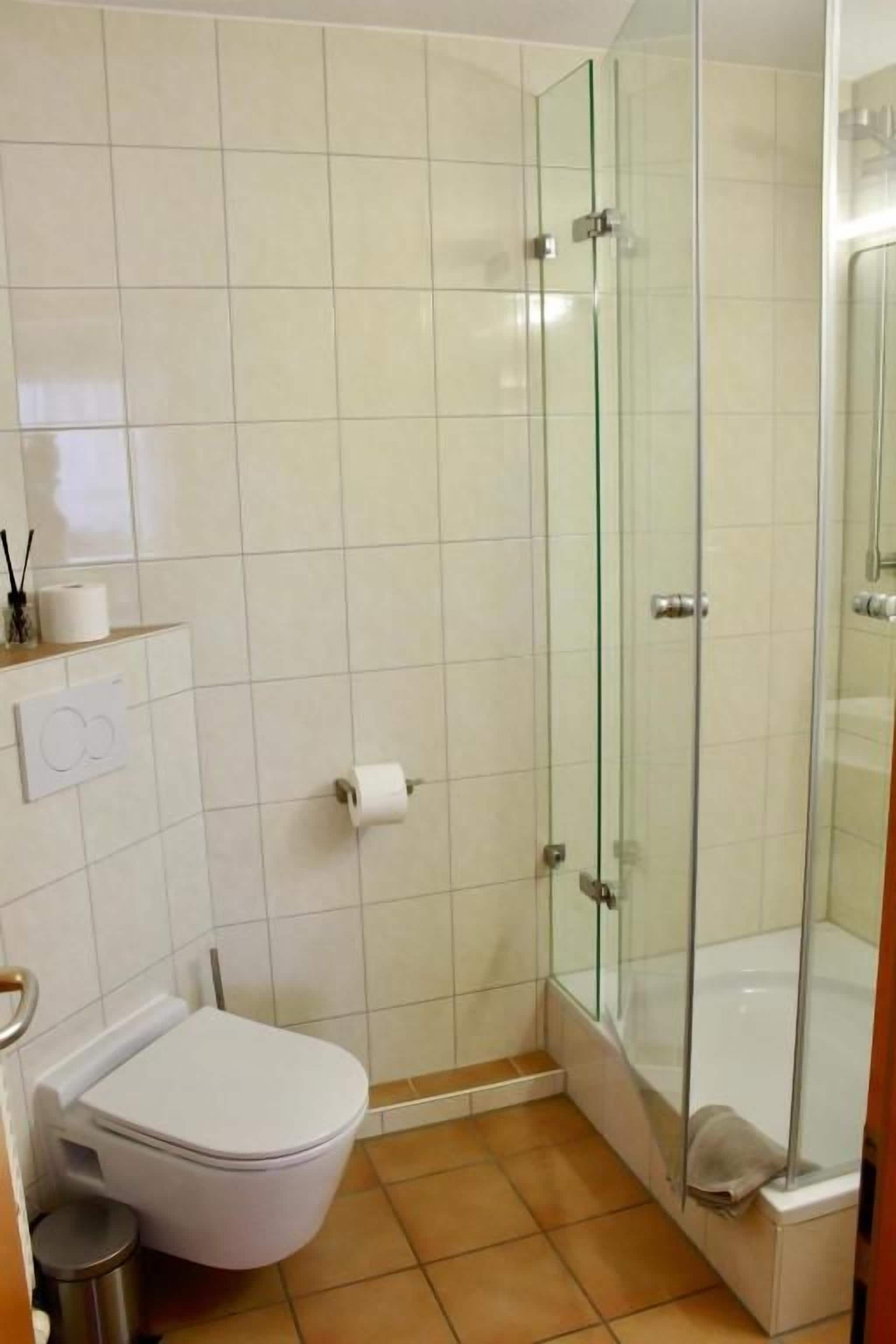 Une salle de bain comprenant des toilettes, une douche en verre et un sol carrelé.
