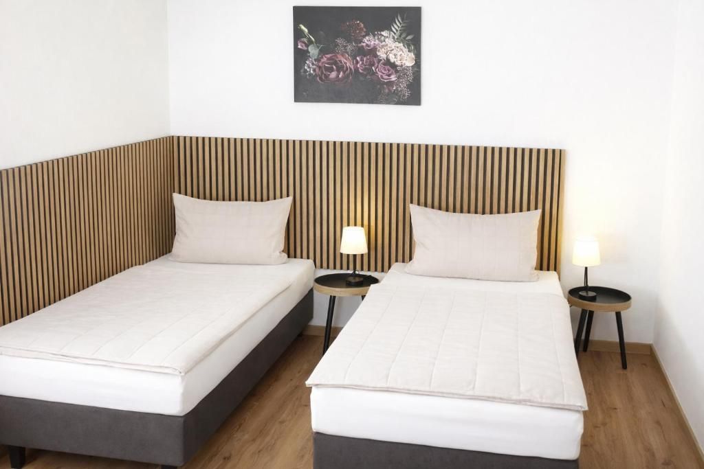 A hotel room with two beds, a wooden slat headboard, bedside lamps, and a floral artwork on the wall.