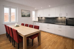 A modern kitchen with white cabinets, a wooden dining table, and red chairs. - Gästehaus Jekle – Zimmer & Ferienwohnungen (Neuburg an der Kammel)