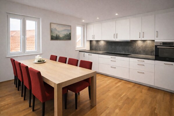 A modern kitchen with white cabinets, a wooden dining table, and red chairs. - Gästehaus Jekle – Zimmer & Ferienwohnungen (Neuburg an der Kammel)