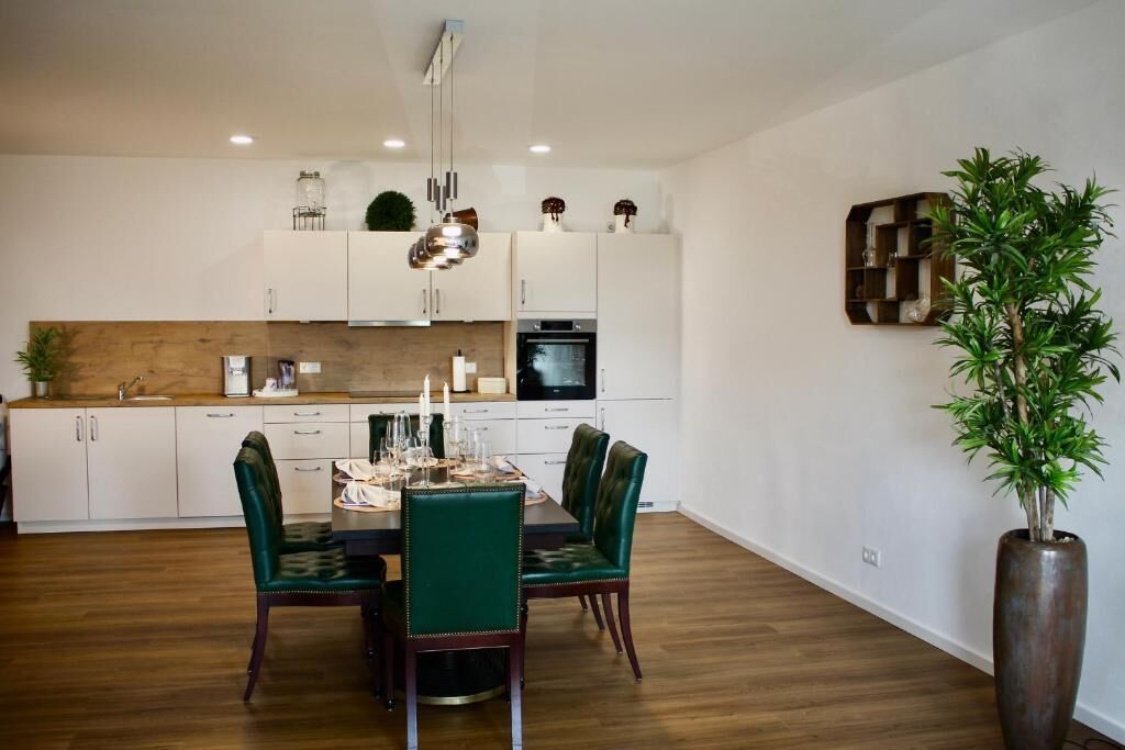 Una cocina moderna con armarios blancos, encimera de madera y una zona de comedor con sillas tapizadas en verde.