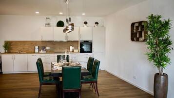 Una cocina moderna con armarios blancos, encimera de madera y una zona de comedor con sillas tapizadas en verde.