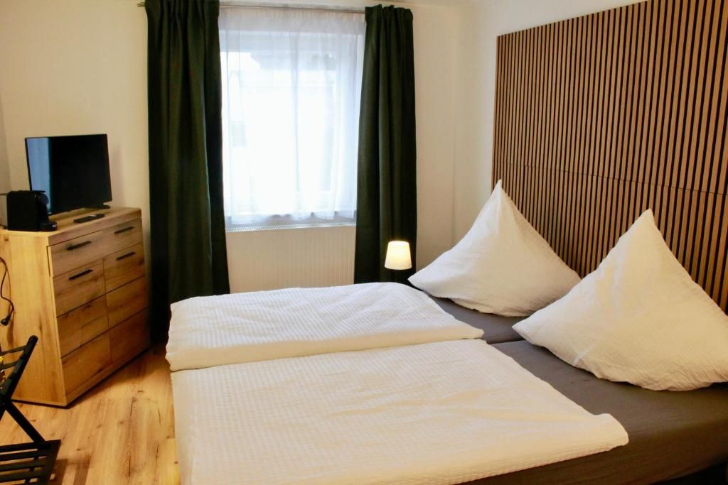 A hotel room with a bed, a TV on a wooden dresser, a window with curtains, and a bedside lamp.
