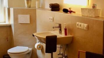 Une salle de bain avec des toilettes, un lavabo et un miroir. Il y a une plante accrochée au mur et un porte-serviettes avec des serviettes.