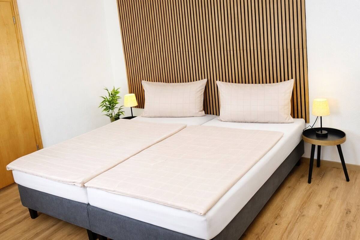 Ein Doppelbett mit Holz-Kopfteil, zwei Nachttische mit Lampen und eine kleine Pflanze auf dem Nachttisch.