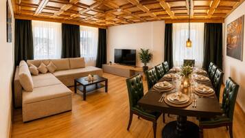 A living room with a sofa, a TV, a dining table set for four, and a wooden ceiling.