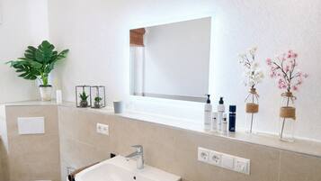 Een badkamer met een wit wastafelmeubel, een spiegel en toiletartikelen op het aanrecht.