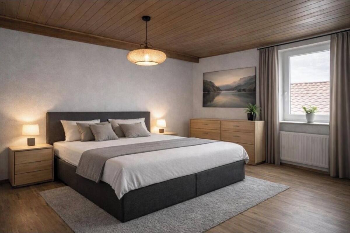 Ein Schlafzimmer mit einem großen Bett, einem Holz-Kopfteil, Nachttischlampen, einem Fenster mit Vorhängen und einem Bild an der Wand.
