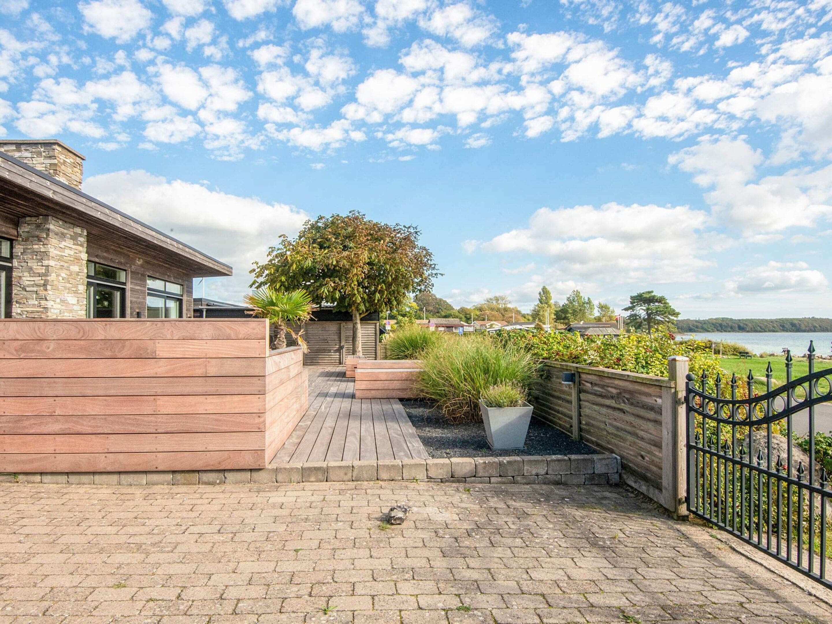 A wooden deck with a stone wall, potted plants, and a view of a lake.