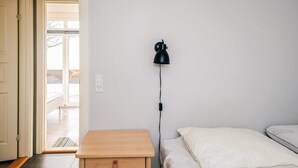 Ett sovrum med en säng, ett nattduksbord, en lampa och en dörr som leder till ett annat rum.