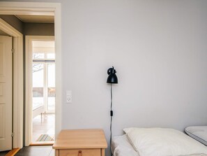 Un dormitorio con cama, mesita de noche, lámpara y una puerta que da a otra habitación.