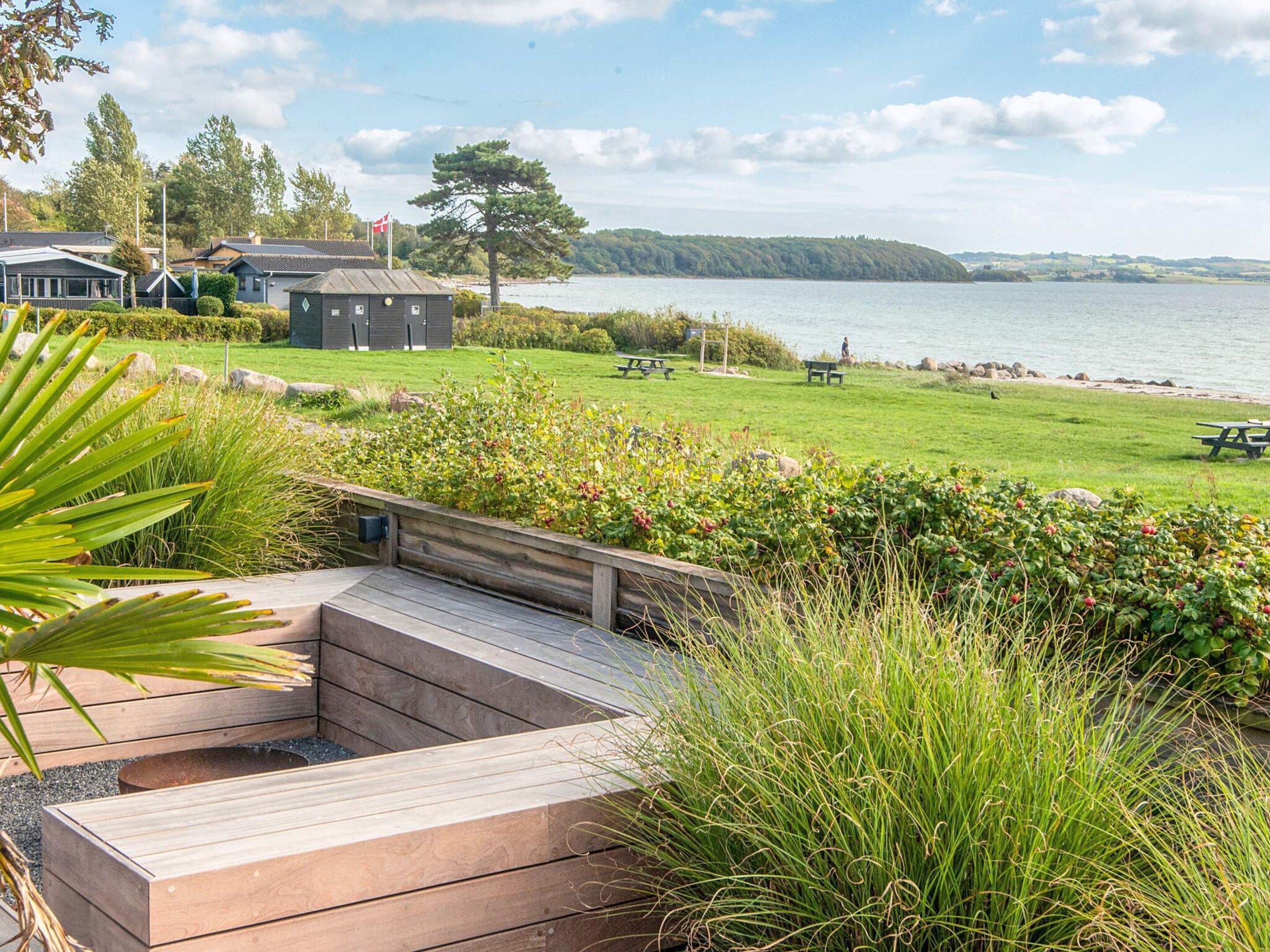 Een vakantiehuis aan het meer met een houten terras, picknicktafels en uitzicht op het water.