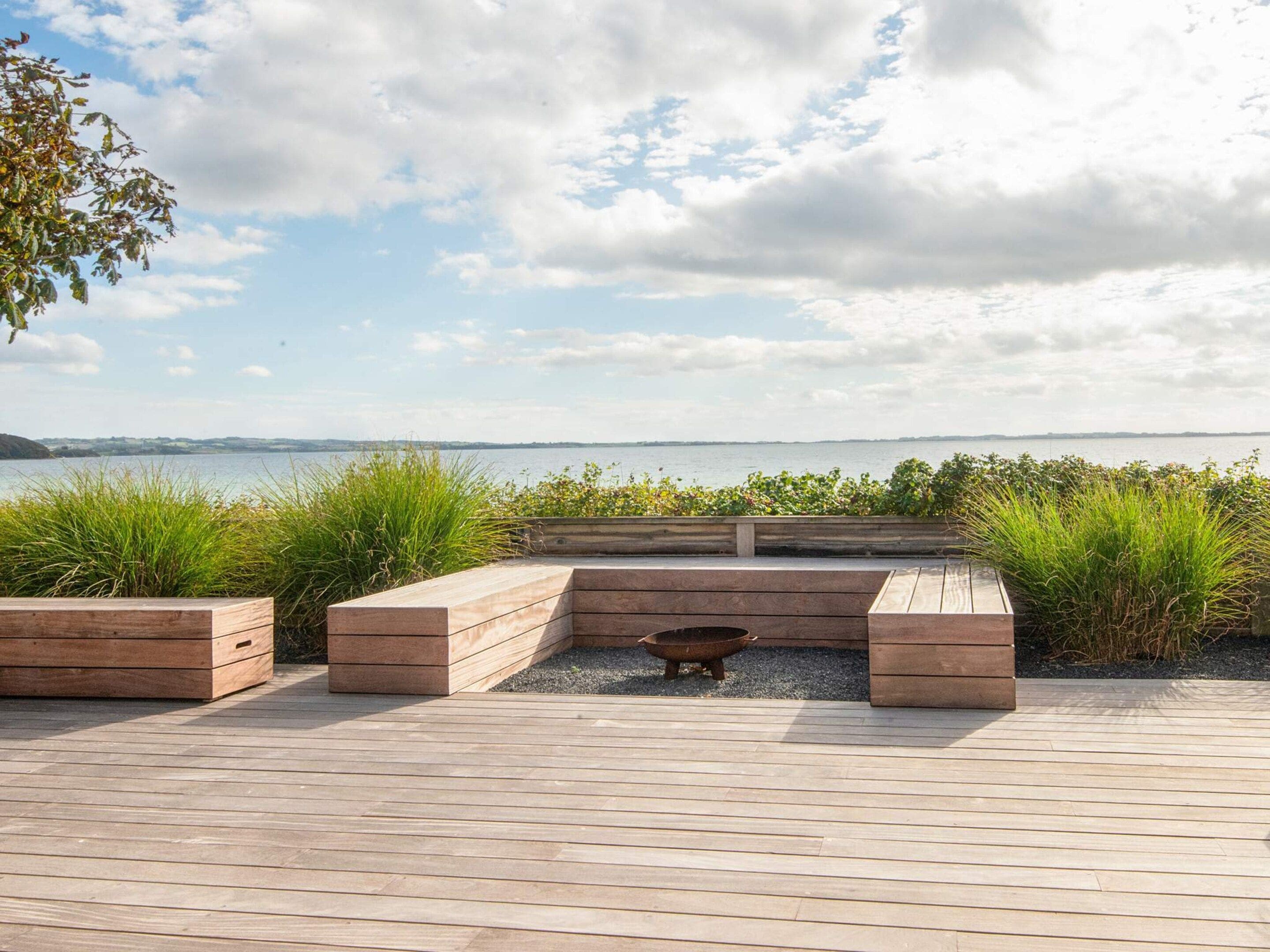 A wooden deck with built-in seating and a fire pit, overlooking a body of water.