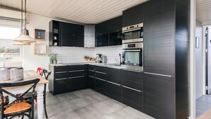 Ett modernt kök med mörka köksskåp, rostfria vitvaror och en matplats med ett träbord och stolar.