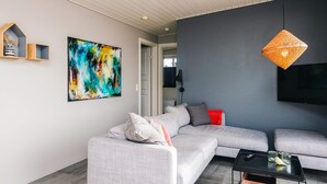 Ett modernt vardagsrum med en grå hörnsoffa, ett svart soffbord, en flätad hänglampa och en stor, abstrakt tavla på väggen.