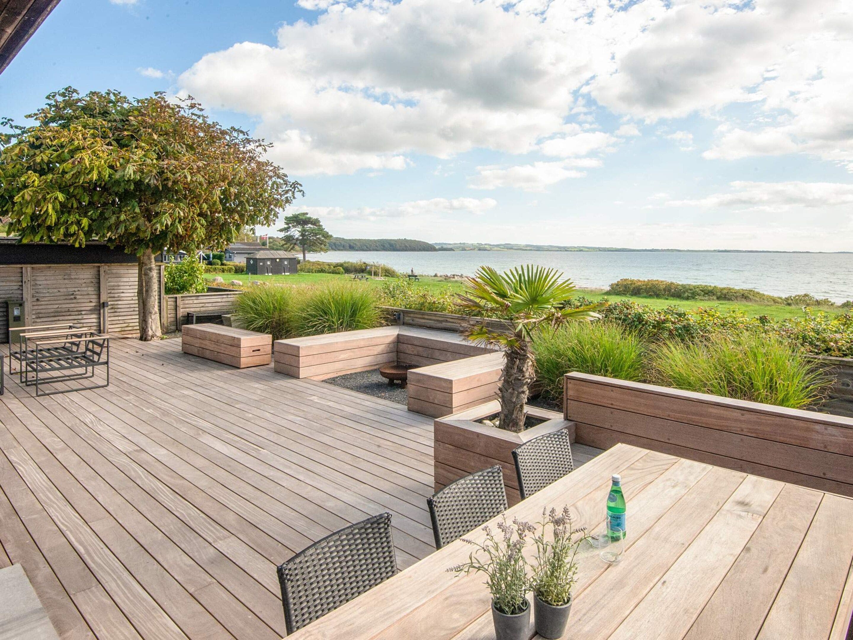 A wooden deck with outdoor seating, a table with potted plants, and a view of the water.