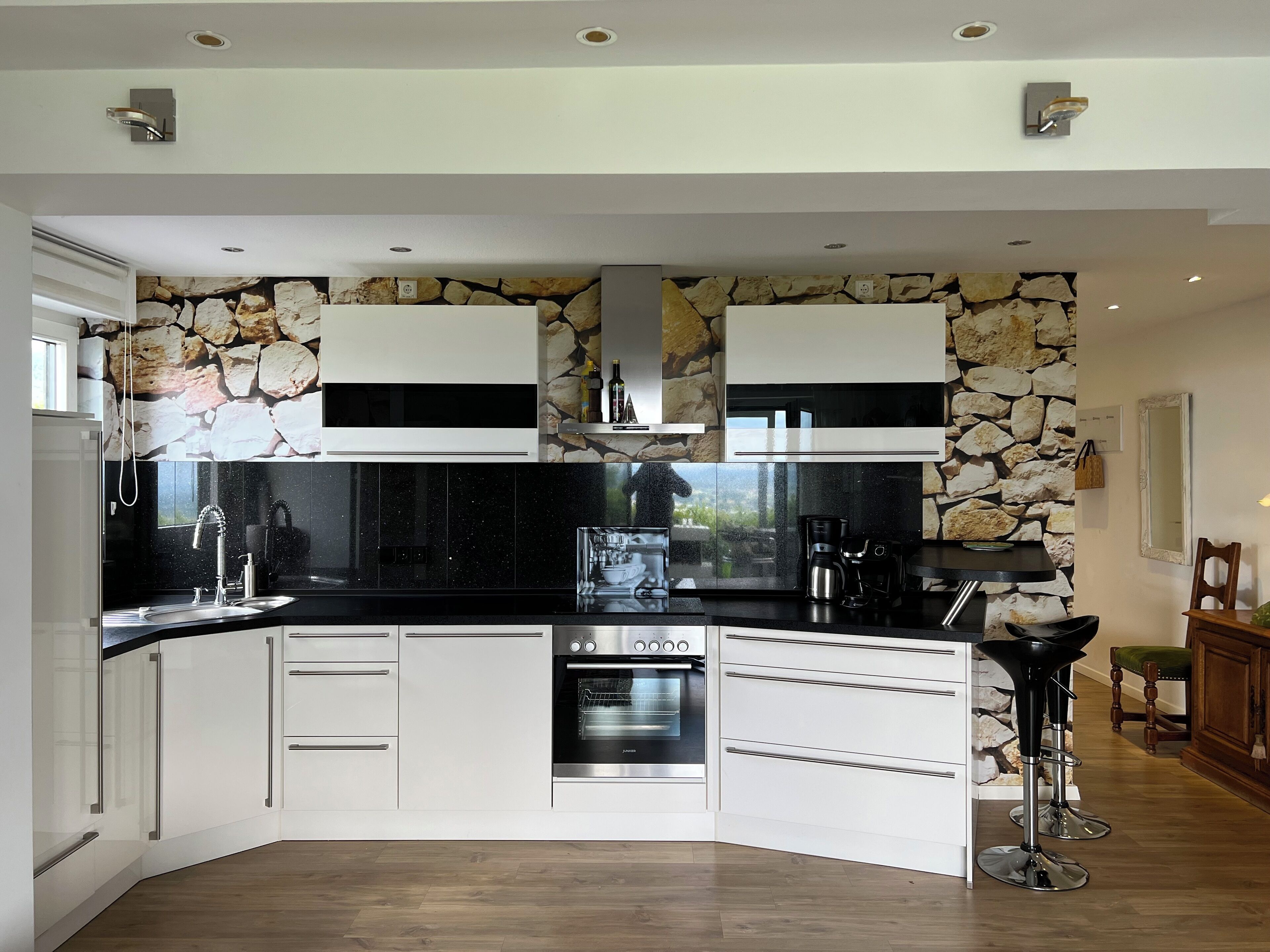 A modern kitchen with white cabinetry, a built-in oven, and a stone accent wall.