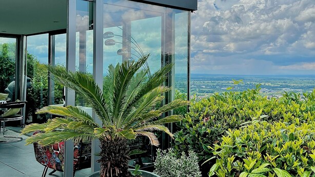 En moderne bygning med store glasruder, udsigt over landskabet og forskellige planter.