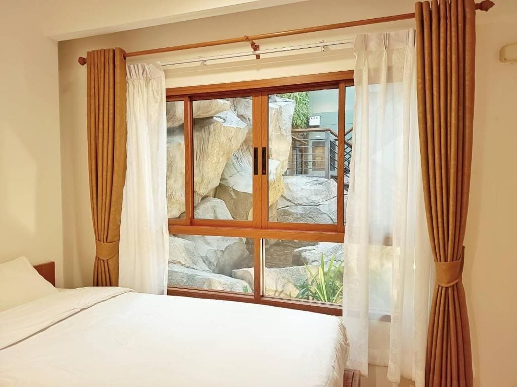 A bedroom with a large window, curtains, and a bed.