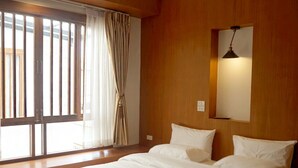 A bedroom with a large bed, wooden walls, a window with curtains, and a wall-mounted light. - Forte Hostel (Chiang Mai)