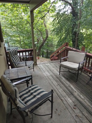 A wooden deck with outdoor furniture, including striped lounge chairs and a sofa, surrounded by trees. - Rendezvous Townhouse on Spring (Eureka Springs)