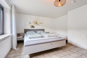 Un dormitorio moderno con cama, mesita de noche, ventana con cortinas y lámpara de techo.